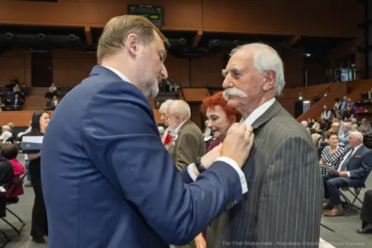 Uroczystość wręczenia odznaczeń, mężczyzna przypina medal do marynarki innego mężczyzny.