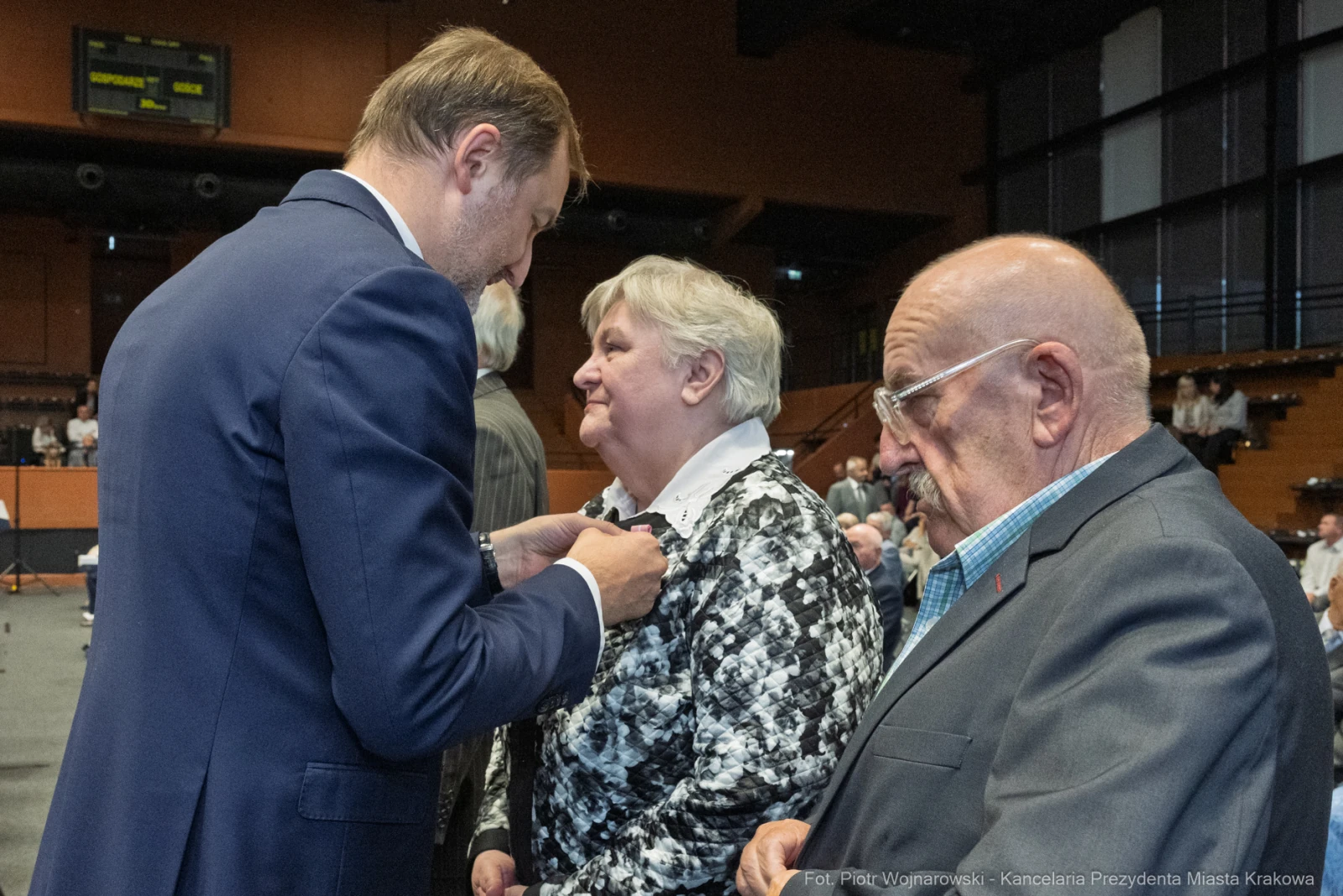 Wręczenie odznaczenia przez mężczyznę starszej kobiecie, obok siedzi starszy mężczyzna.  Autor: Piotr Wojnarowski