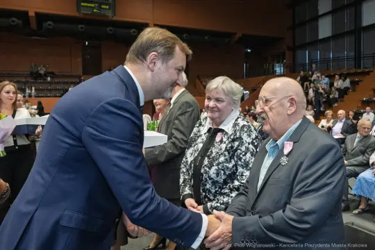 Wręczenie nagród w uroczystej atmosferze, uściski dłoni i uśmiechy uczestników.