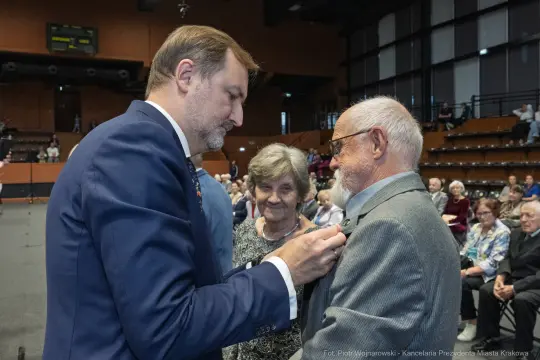 Wręczenie odznaczenia mężczyźnie przez urzędnika, w tle starsza para.