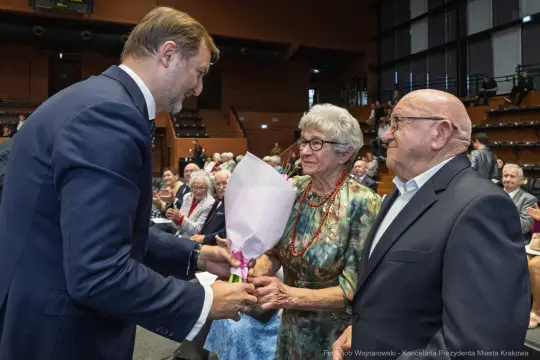 Uroczystość wręczenia kwiatów parze starszych ludzi.