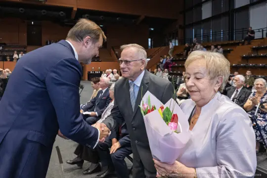Uścisk dłoni, mężczyzna z bukietem kwiatów, starsza para w eleganckich strojach.