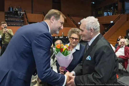Uroczystość wręczenia kwiatów starszemu mężczyźnie przez młodszego mężczyznę.