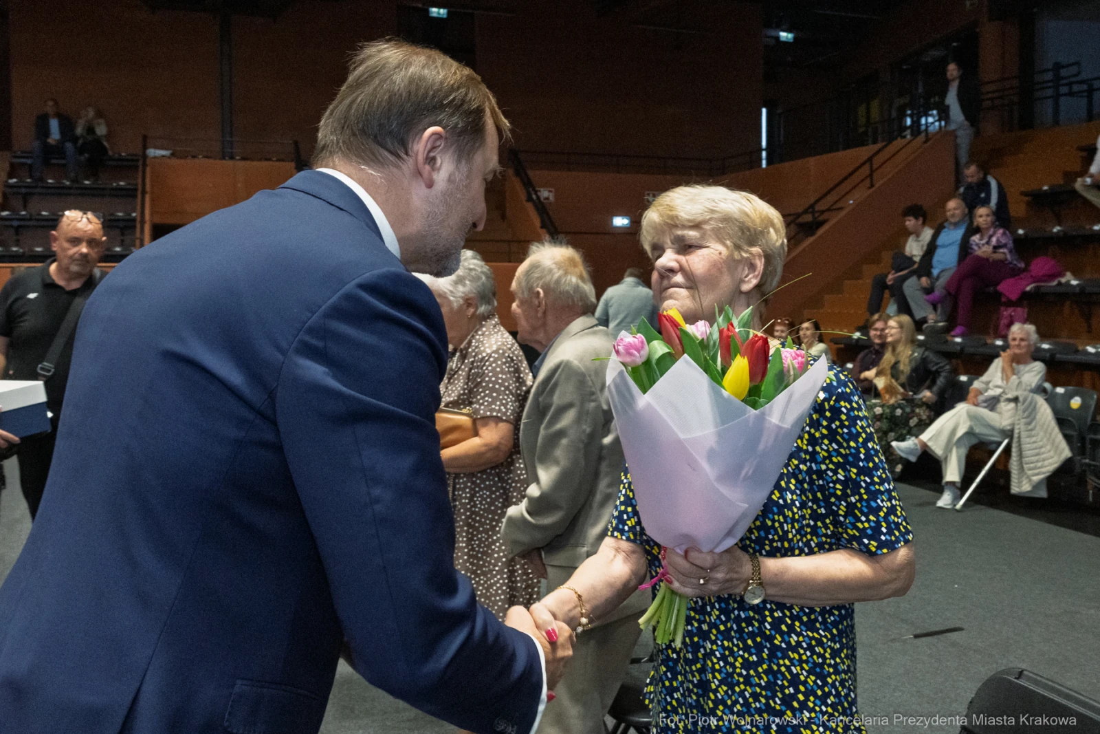Mężczyzna wręcza bukiet kwiatów starszej kobiecie podczas uroczystości.  Autor: Piotr Wojnarowski