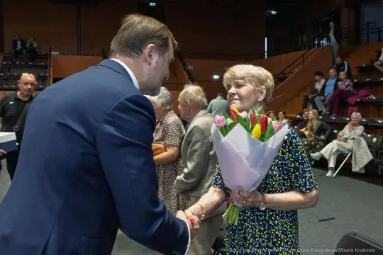 Mężczyzna wręcza bukiet kwiatów starszej kobiecie podczas uroczystości.