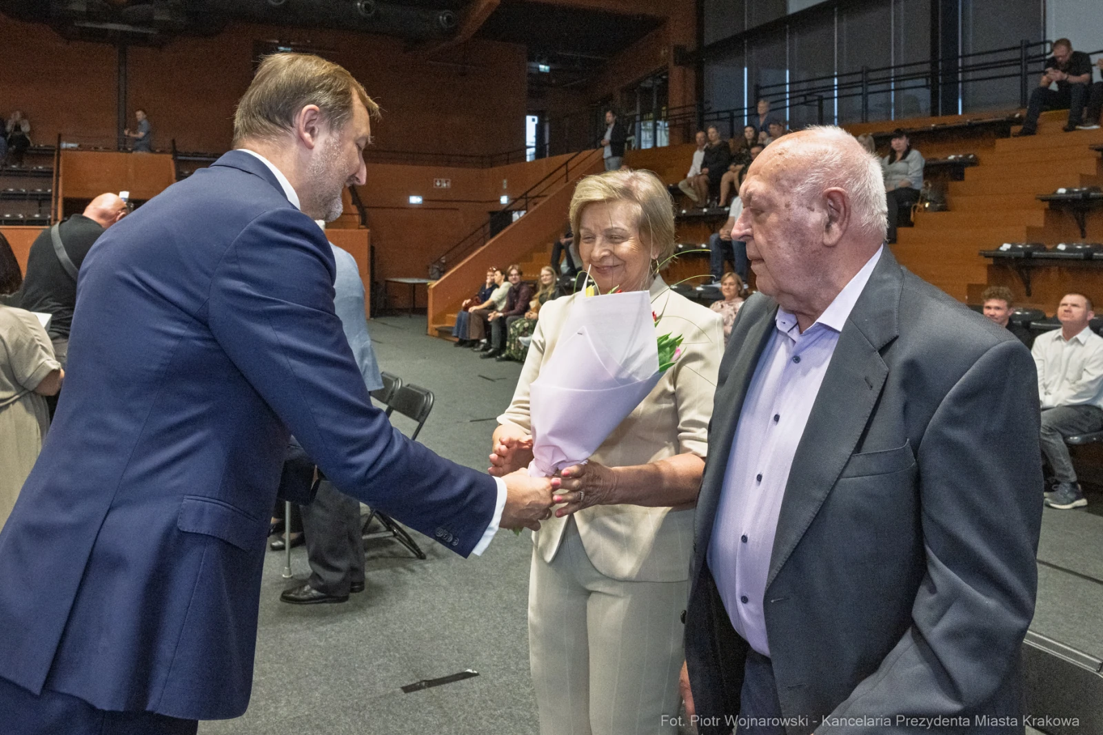 Uroczystość wręczenia kwiatów dwóm osobom przez mężczyznę w garniturze.  Autor: Piotr Wojnarowski