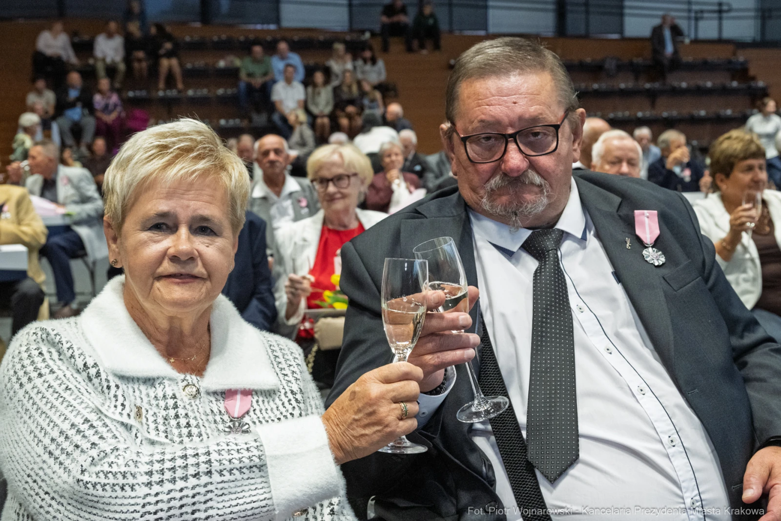 Para osób w eleganckich strojach wznoszą kieliszki w towarzystwie innych gości.  Autor: Piotr Wojnarowski