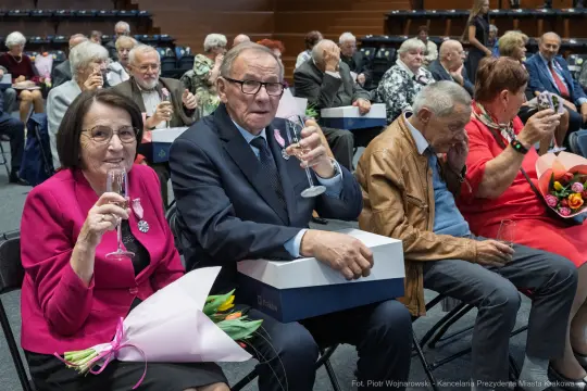 Uroczystość z jubilatami, kwiaty i szampan w rękach gości.