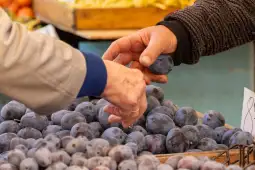 Ręce wymieniające śliwki na targu.