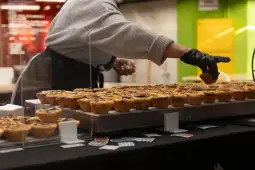 Osoba nakładająca ciasto na talerze z tartaletkami w cukierni.