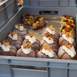 Pyszne croissanty z bitą śmietaną i owocami w pojemniku.