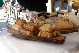 Serowe wyroby na drewnianej desce, różne kształty i rodzaje, z etykietami.