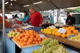 Stragan z owocami, w tym pomarańcze, winogrona i jagody, oraz klienci wybierający produkty.