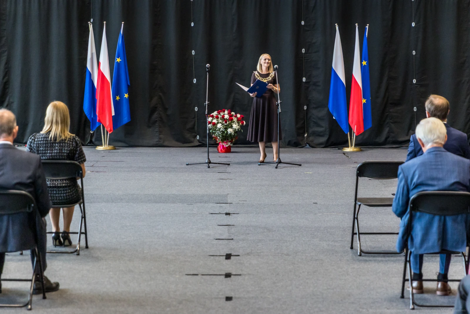 Kobieta w eleganckiej sukience przemawia na tle flag Polski i Unii Europejskiej.  Autor: Bogusław Świerzowski
