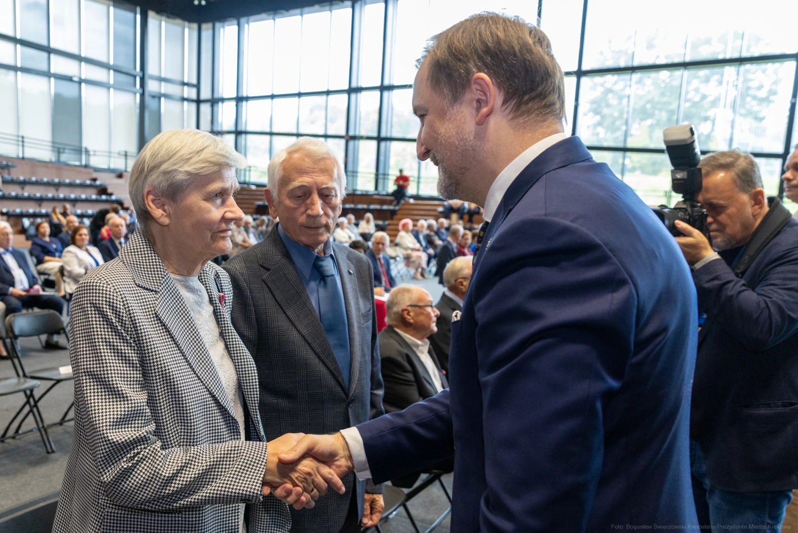 Spotkanie dwóch osób z mężczyzną w garniturze, uściski dłoni, w tle publiczność.  Autor: Bogusław Świerzowski
