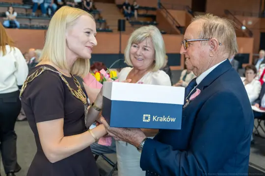 Wręczenie nagrody przez przedstawicielkę miasta Kraków mężczyźnie w garniturze, obok uśmiechająca się kobieta.