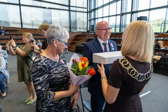 Uroczystość wręczenia nagrody z kwiatami i uśmiechami uczestników.