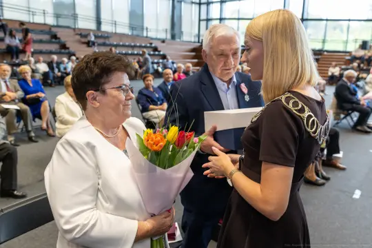 Kobieta z bukietem tulipanów rozmawia z inną osobą w towarzystwie mężczyzny. W tle zgromadzenie ludzi.