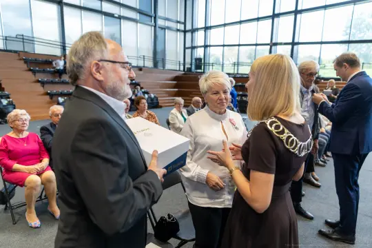 Wręczenie odznaczeń w trakcie uroczystości, uczestnicy w formalnych strojach.