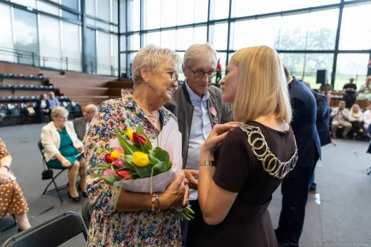 Spotkanie dwóch kobiet z bukietem tulipanów oraz mężczyzny w tle.
