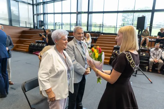 Kobieta wręcza bukiet tulipanów starszej parze podczas uroczystości.