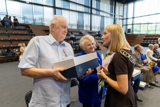 Uroczystość wręczenia odznaczeń, mężczyzna z medalem odbiera nagrodę od kobiety.