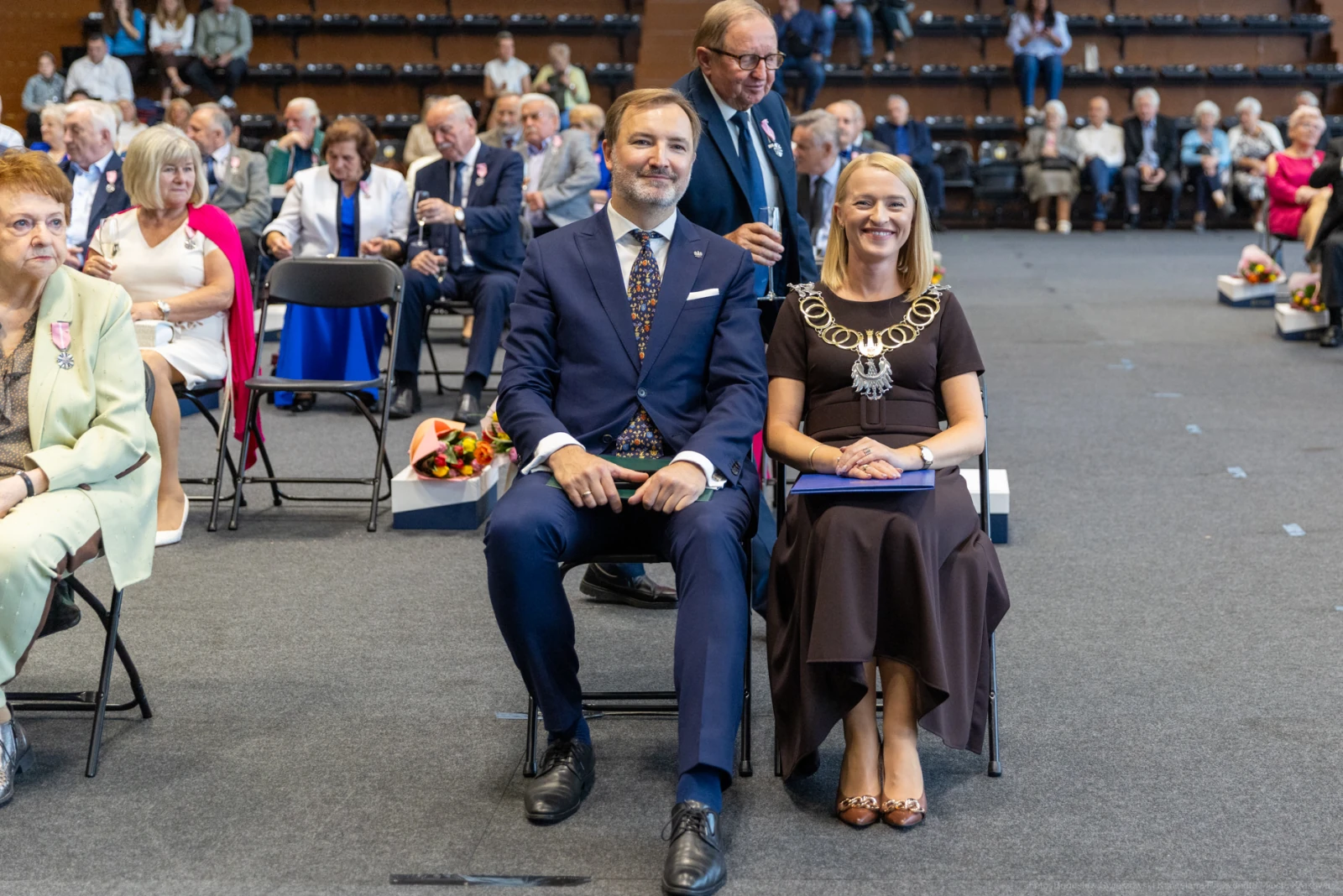 Uroczystość z uczestnikami siedzącymi na krzesłach, w tle widoczni goście.  Autor: Bogusław Świerzowski