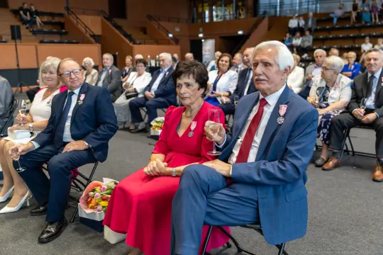 Uczestnicy uroczystości siedzący na widowni, niektórzy z odznaczeniami.