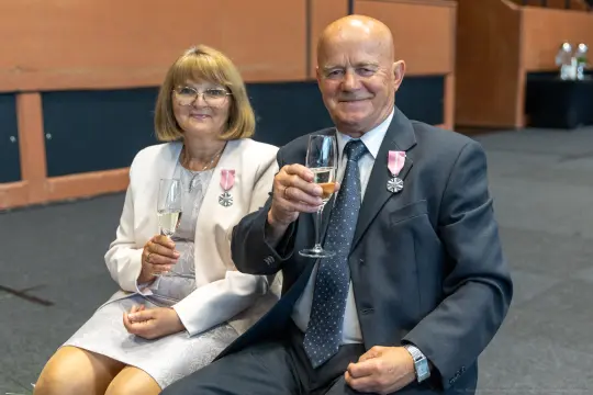 Mężczyzna i kobieta siedzący, trzymający kieliszki z szampanem, ubrani elegancko.