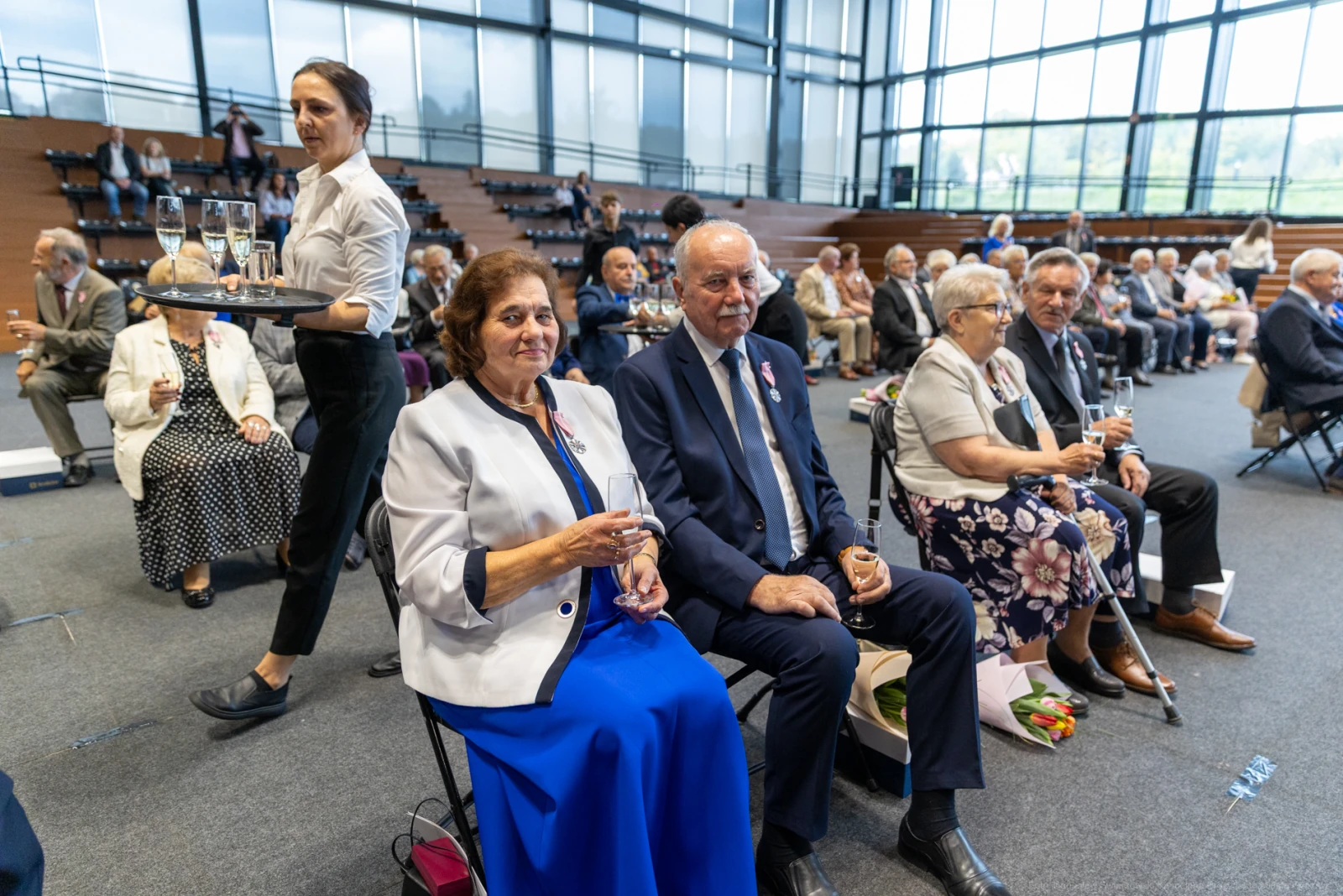 Uczestnicy uroczystości siedzą na widowni, trzymając kieliszki z napojami.  Autor: Bogusław Świerzowski