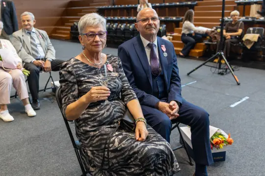 Uroczystość wręczenia odznaczeń, para siedząca na widowni z kieliszkami.