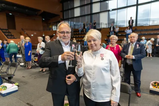Para w eleganckich strojach wznosi kieliszki w trakcie uroczystości.