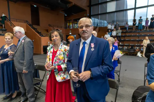Uroczystość z gośćmi w eleganckich strojach, trzymającymi kieliszki.