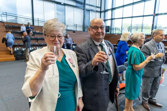 Para osób w eleganckich strojach wznoszą kieliszki w trakcie uroczystości.