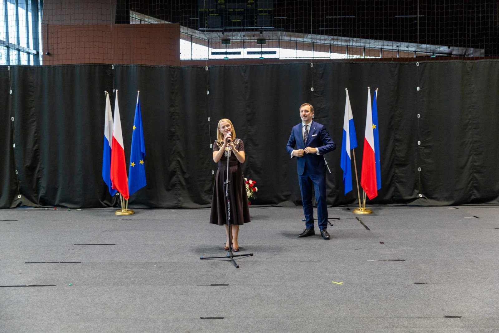 Kobieta w czarnej sukience przemawia na tle flag Polski, Rosji i Unii Europejskiej.  Autor: Bogusław Świerzowski