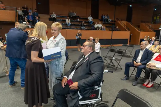 Uroczystość wręczenia nagród, osoby w strojach formalnych, widoczna scena z publicznością.