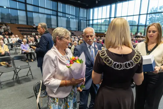 Uroczystość wręczenia nagród z udziałem osób z kwiatami i odznaczeniami.