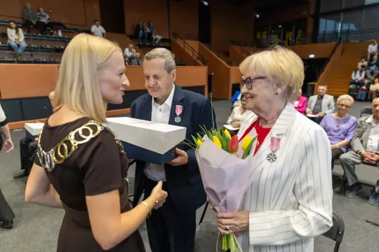 Uroczystość wręczenia odznaczeń, osoby z kwiatami i medalami.