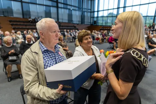 Mężczyzna otrzymuje prezent od kobiety podczas uroczystości w sali pełnej osób.