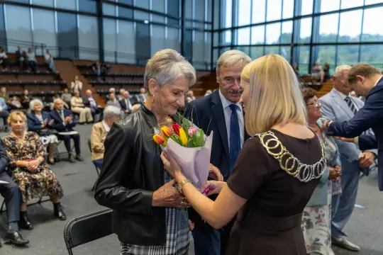 Kobieta otrzymuje bukiet tulipanów podczas uroczystości w sali pełnej gości.