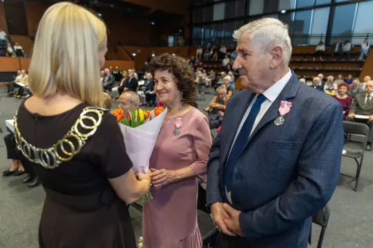 Uroczystość wręczenia odznaczeń, kobieta z bukietem tulipanów rozmawia z mężczyzną.
