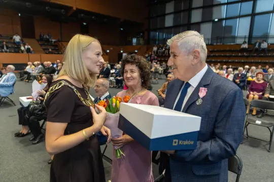 Wręczenie nagród w Krakowie, uśmiechnięci laureaci z kwiatami i prezentem.