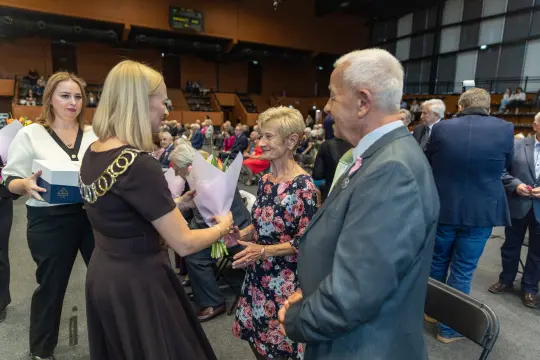 Wręczenie kwiatów podczas uroczystości, uczestnicy w formalnych strojach.