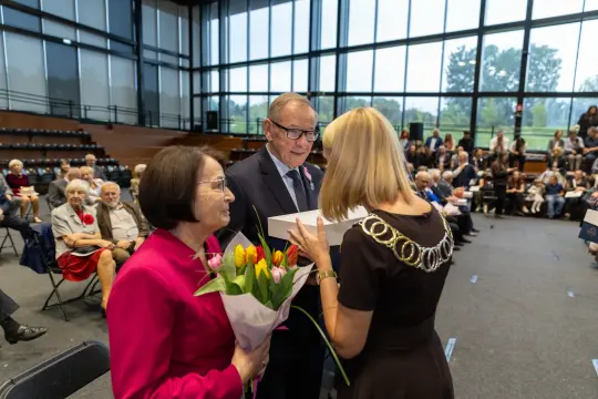Uroczystość wręczenia nagrody z bukietem kwiatów i uśmiechniętymi uczestnikami.