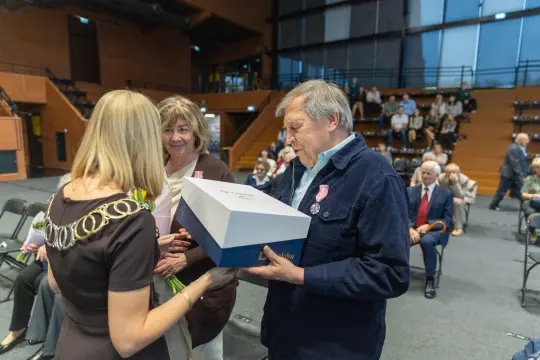 Wręczenie nagrody mężczyźnie przez dwie kobiety w sali pełnej widzów.