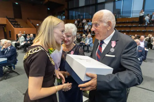 Uroczystość wręczenia nagród, uśmiechnięte osoby w eleganckich strojach.