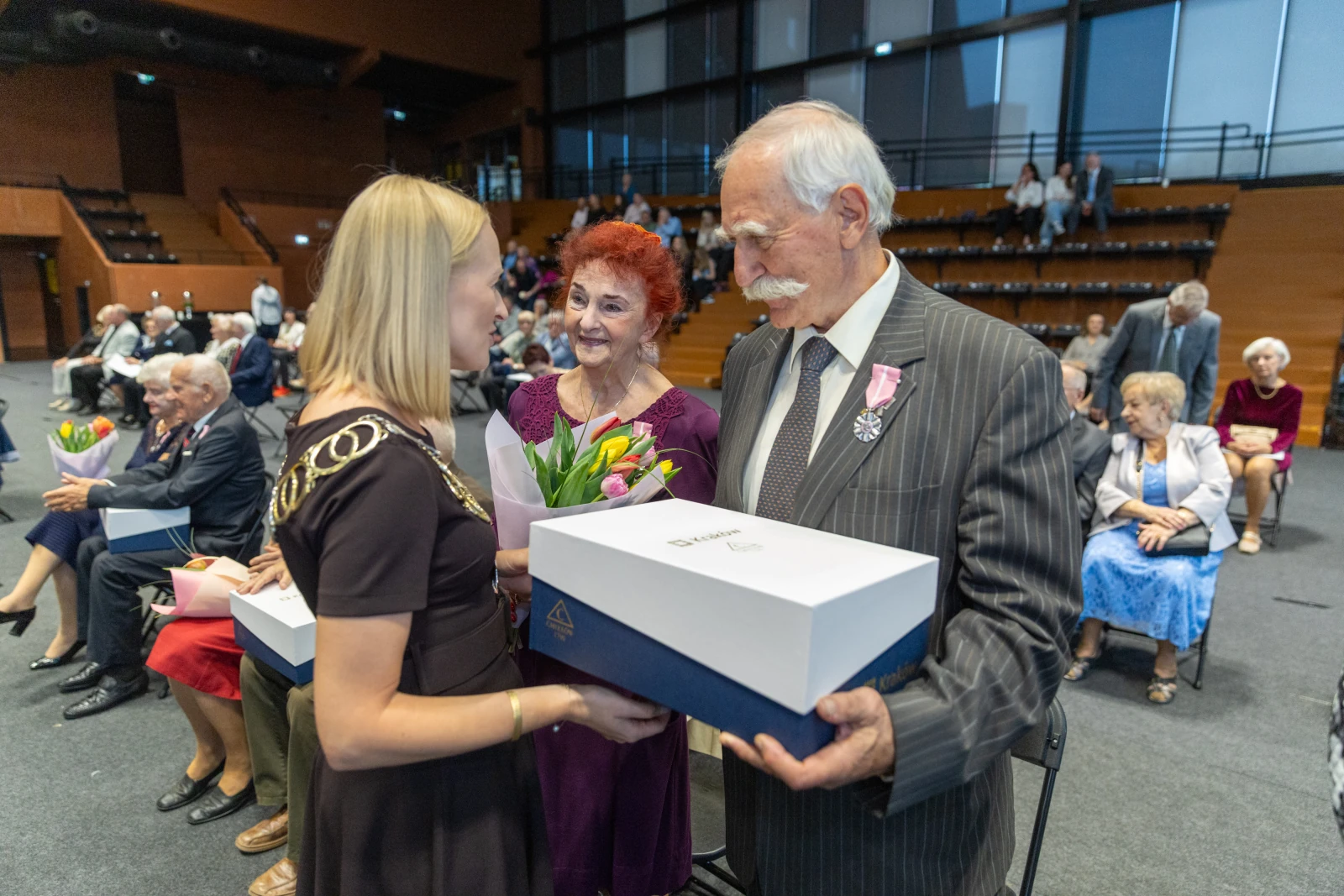 Wręczenie nagród seniorom podczas uroczystości z kwiatami i uśmiechami.  Autor: Bogusław Świerzowski