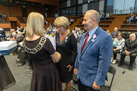 Uroczystość wręczenia odznaczeń w sali z publicznością.