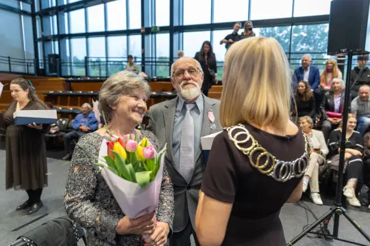 Uroczystość wręczenia odznaczeń, uśmiechnięte twarze, bukiet tulipanów.