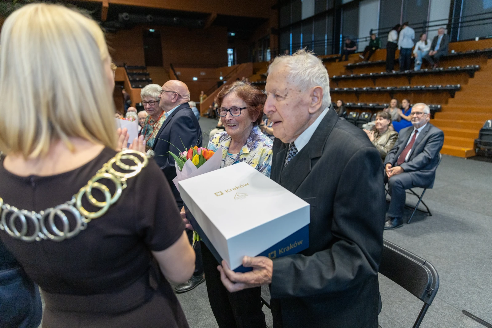 Uroczystość wręczenia nagrody starszemu mężczyźnie i kobiecie z bukietem kwiatów.  Autor: Bogusław Świerzowski